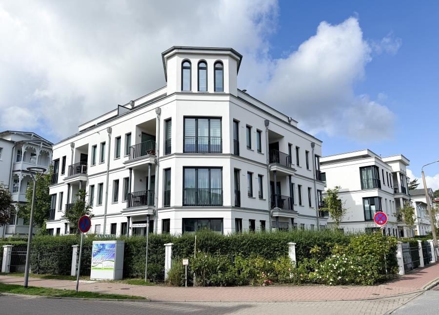 Moderne weiße Wohnanlage mit Balkonen und großen Fenstern unter blauem Himmel.
