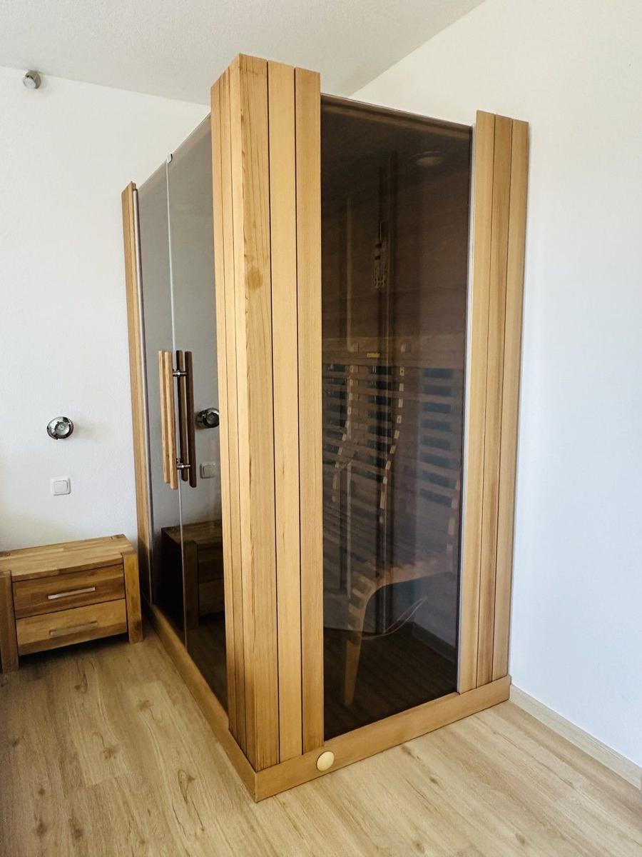 Dampfsauna mit Holzrahmen und Glaswand. Nebenbei steht ein kleiner Holzschrank.