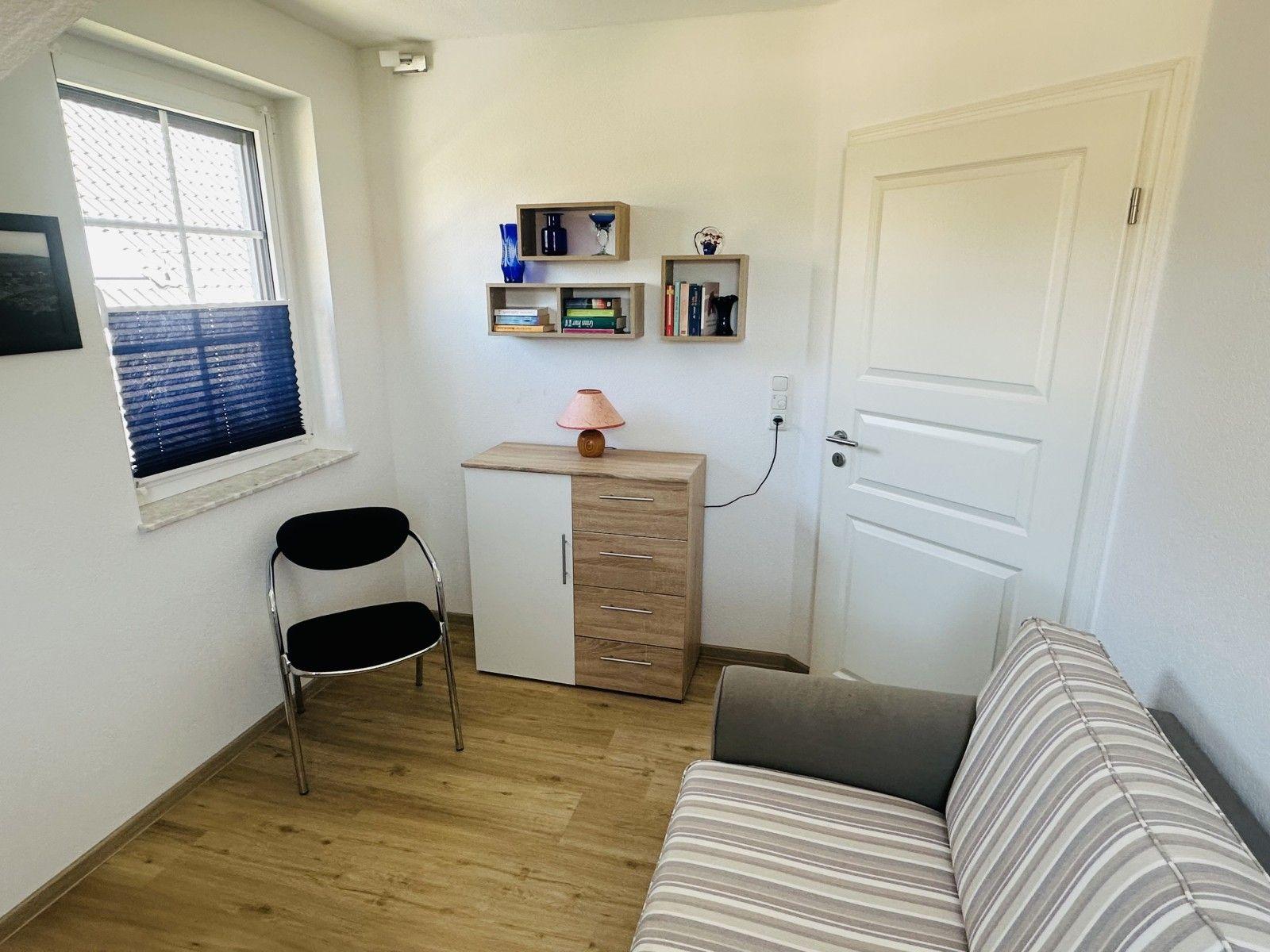Ein Raum mit Sofa, Stuhl, Schrank und Fenster mit Jalousie.