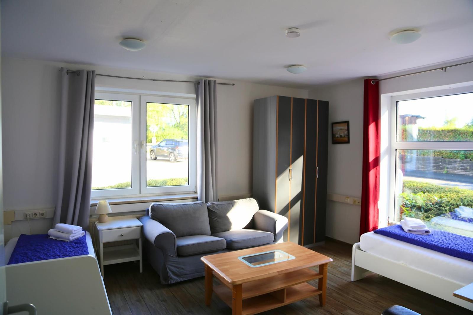 Zimmer mit Sofa, zwei Betten und Fenstern mit Blick nach außen.