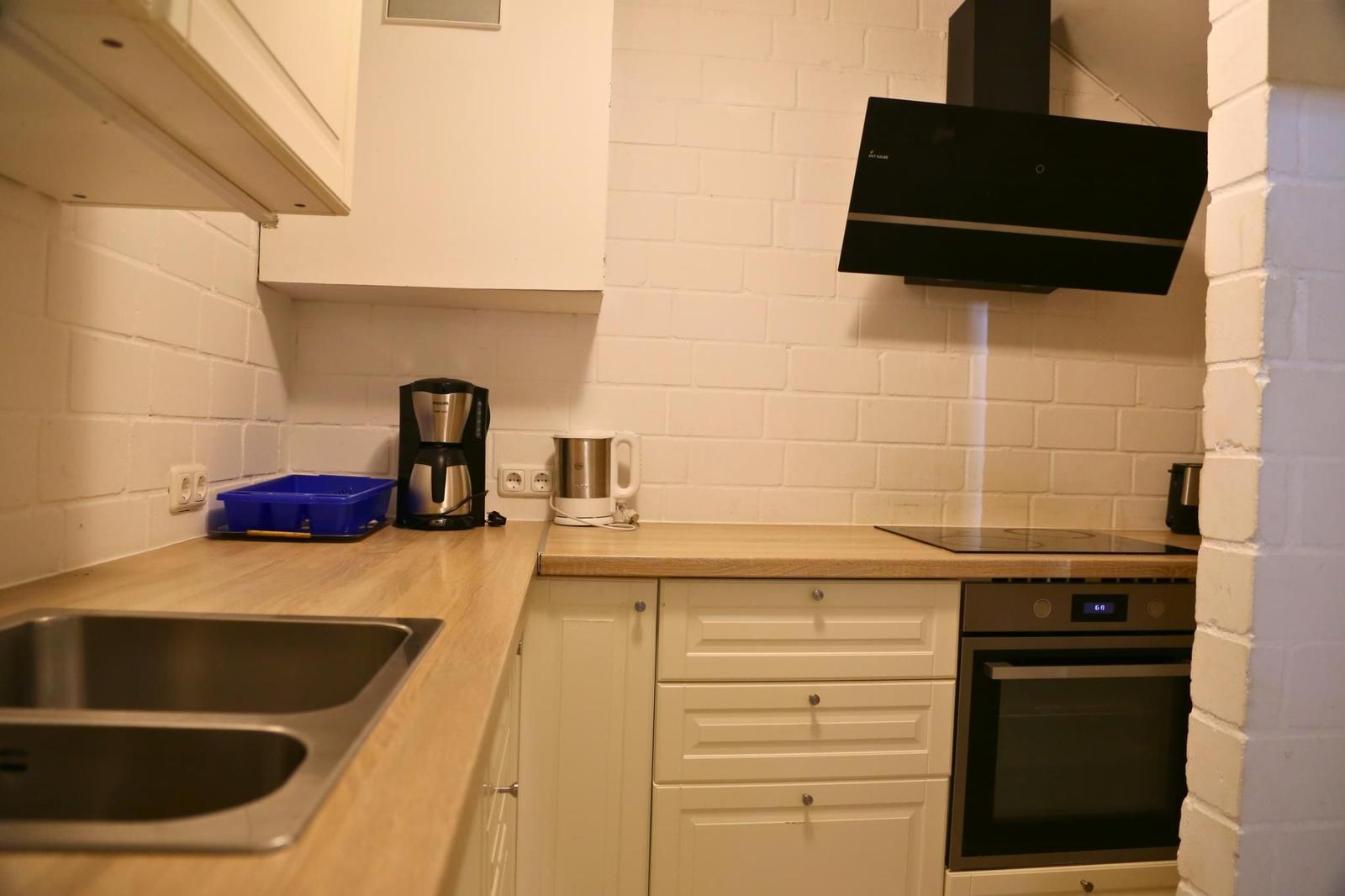 Küche mit Arbeitsplatte, Spüle, Kaffeemaschine und Backofen an weißer Ziegelwand.