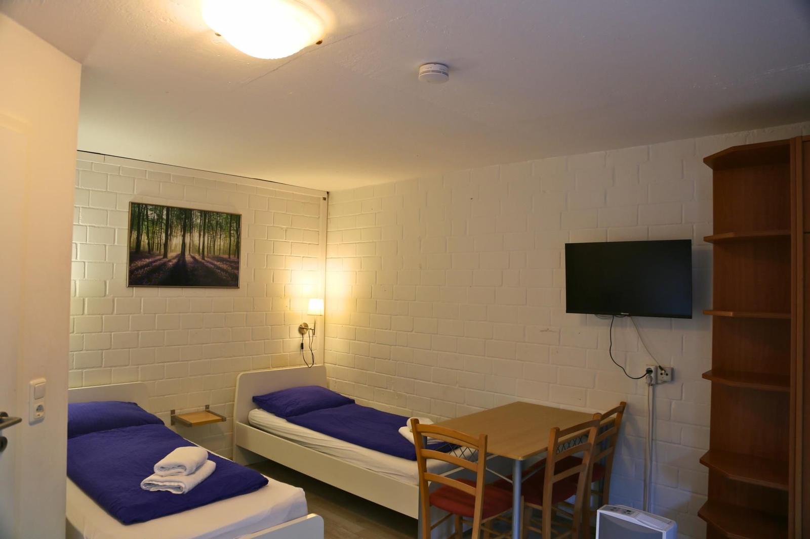 Zwei Betten, Tisch mit Stühlen, Wandbild und Fernseher an der Wand.