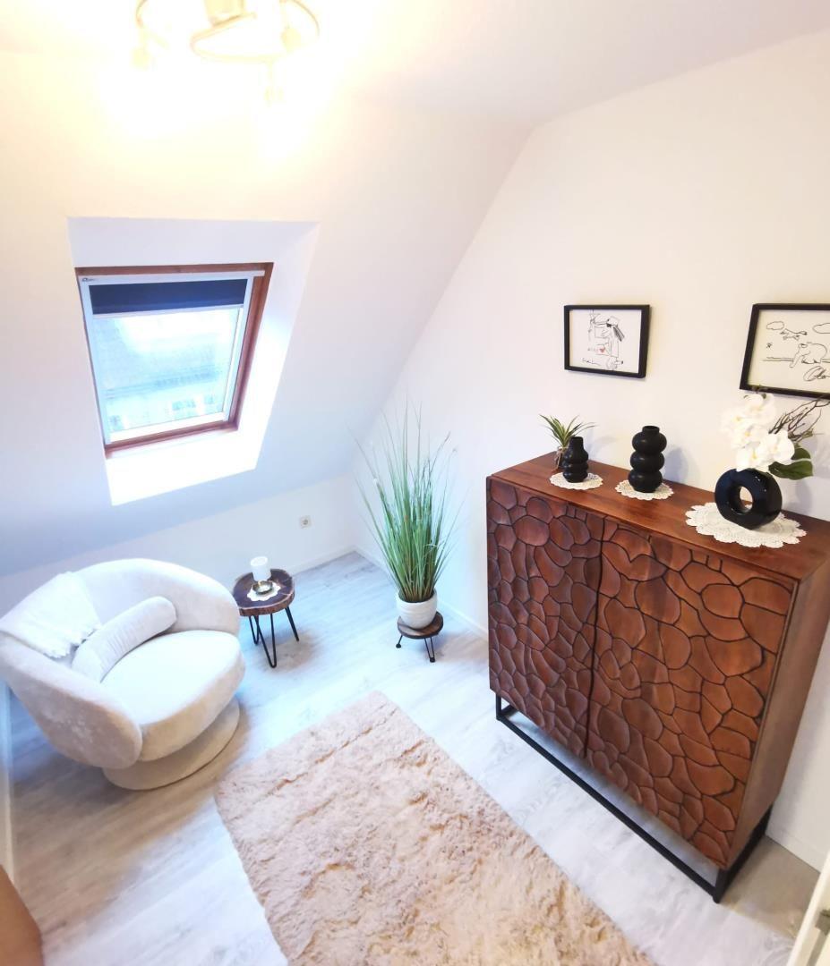 Ein Schlafzimmer mit Dachschräge, weißer Couch, Holzschrank und Fenster.