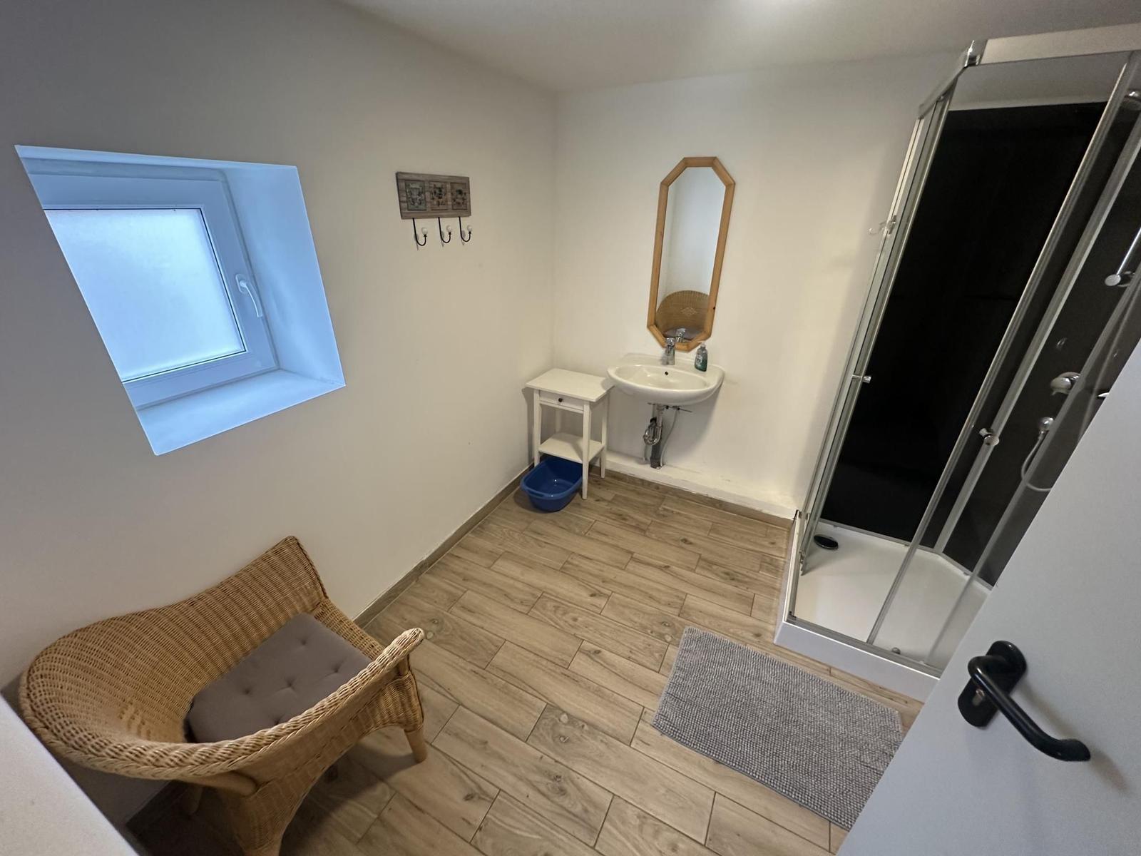 Badezimmer mit Dusche, Waschbecken und Sitzgelegenheit.