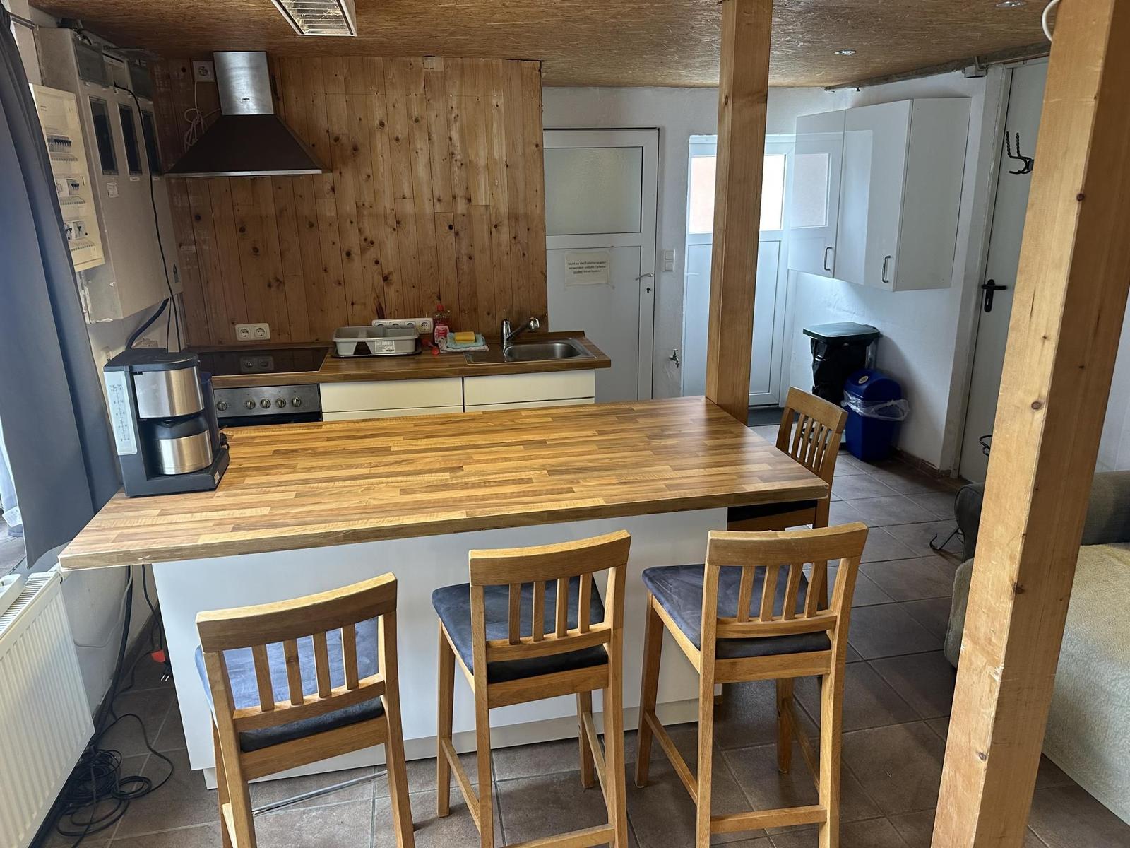 Küche mit Holztheke und Stühlen, Hintergrund Holzwand und weiße Schränke