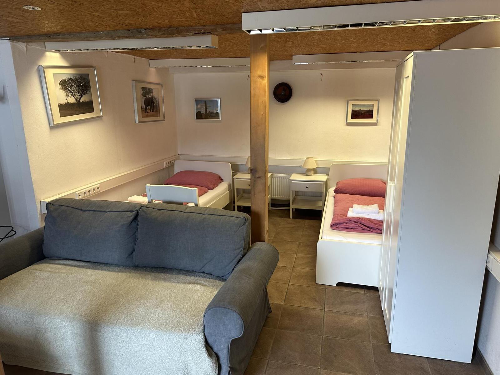 Wohnbereich mit Sofa und zwei Betten im Hintergrund.