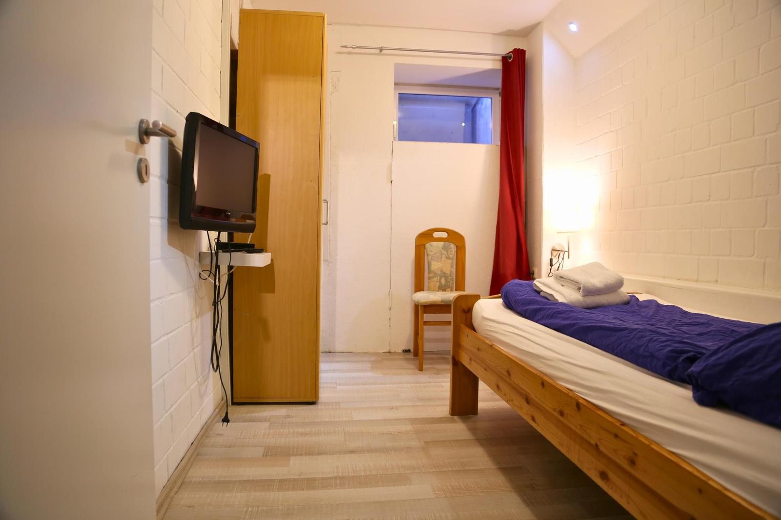 Schlafzimmer mit Bett, Fernseher und Stuhl. Wandgestellte TV und Holzmöbel.