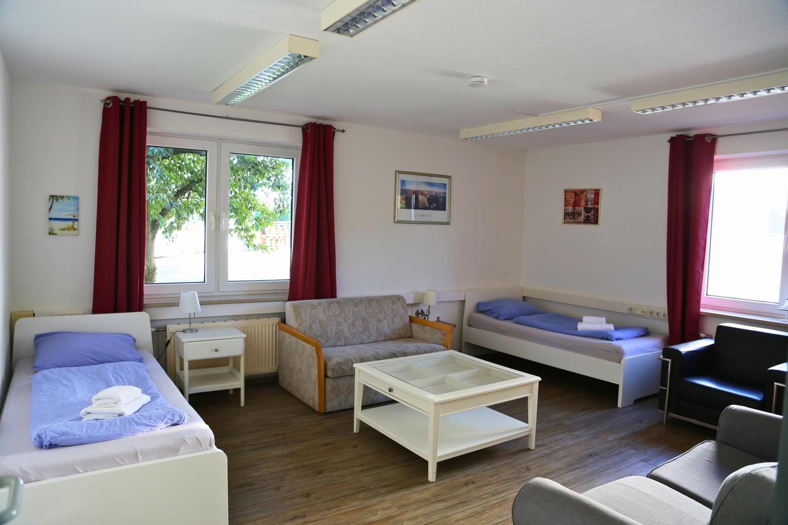 Zimmer mit zwei Betten, Sofa, Couchtisch und Fenstern mit roten Vorhängen.