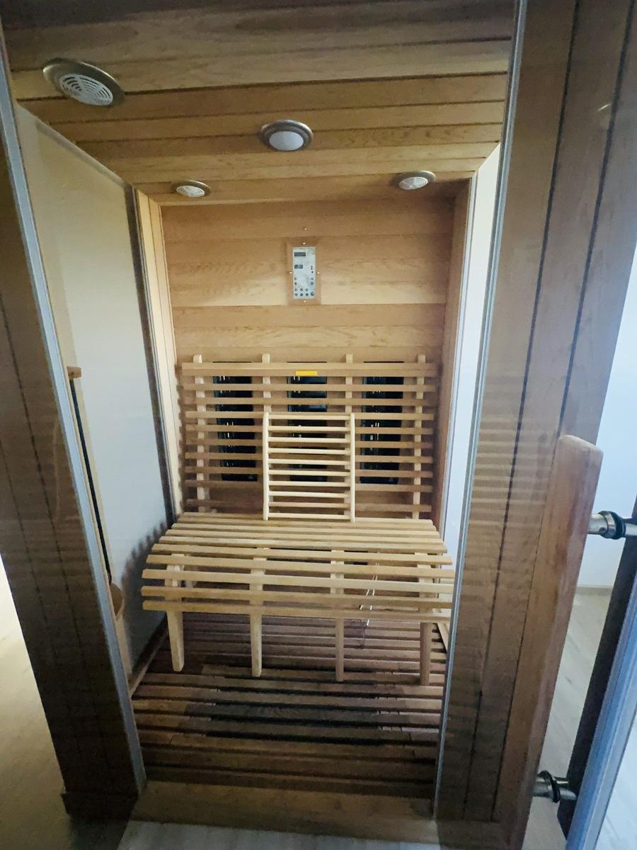 Innere Ansicht einer Holzsauna mit Sitzbank und Steuerungseinheit.