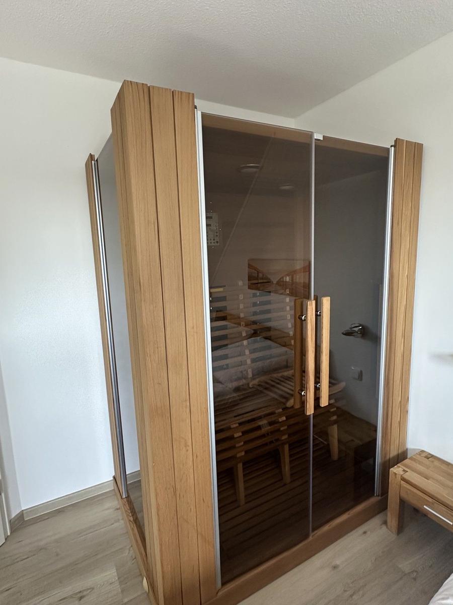 Eine Sauna mit Holzrahmen und Glasfront, zwei Bänke und ein kleiner Holztisch daneben.