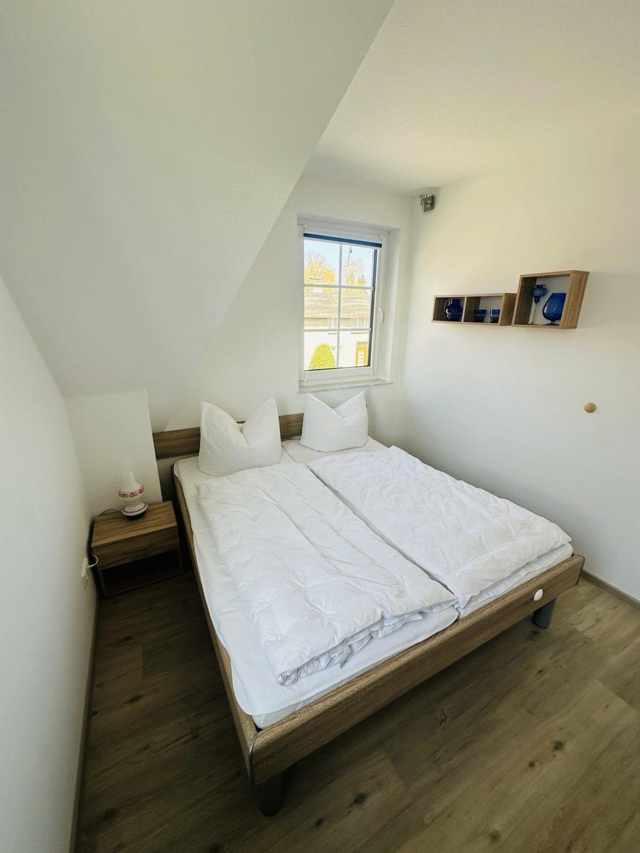 Doppelbettzimmer mit Holzboden, Fenster und Wandregal mit blauen Vasen.