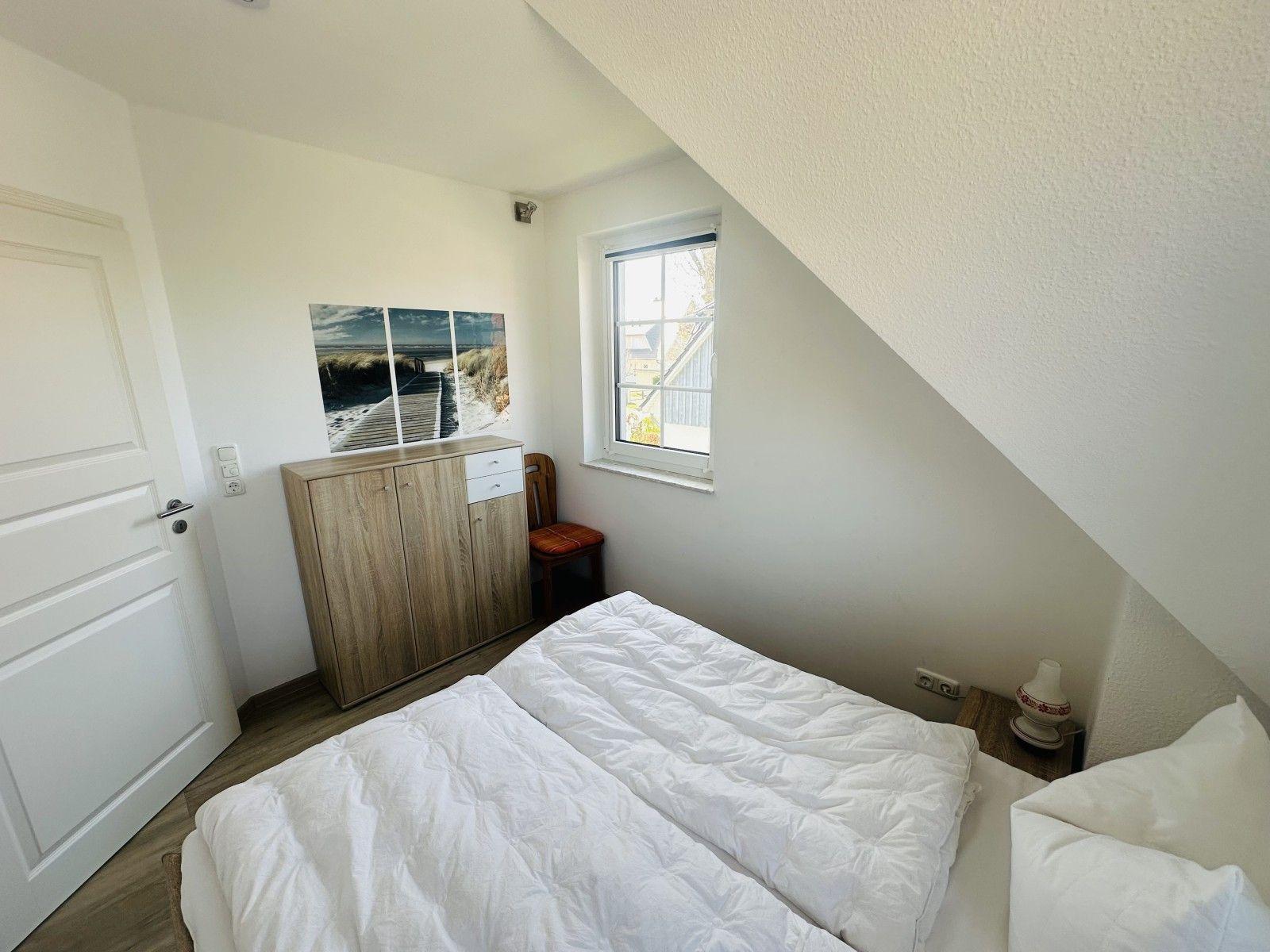Schlafzimmer mit Dachschräge, Bett, Schrank und Fenster.