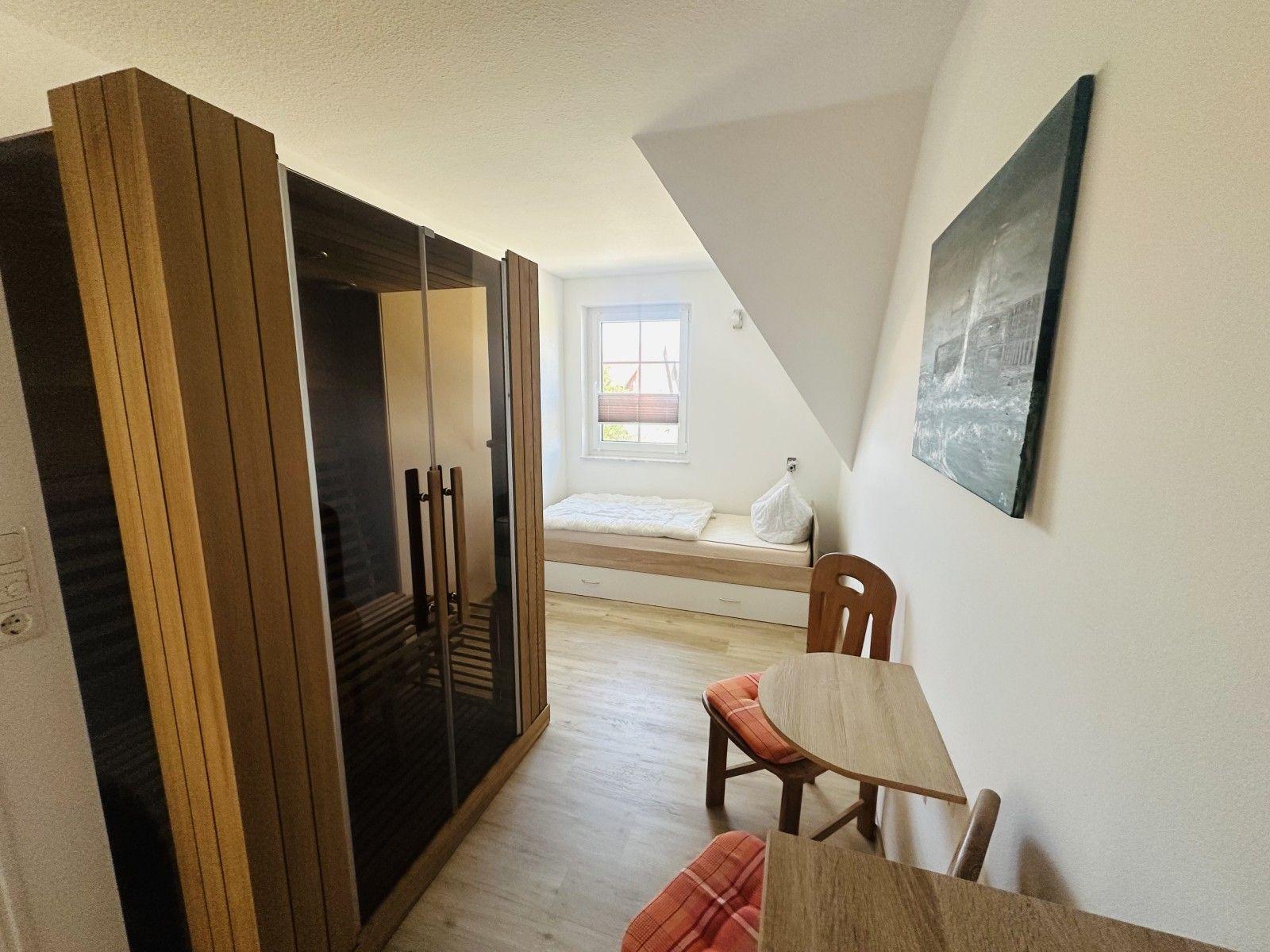 Zimmer mit Dachschrägen, Bett, Tisch, Stuhl und Sauna