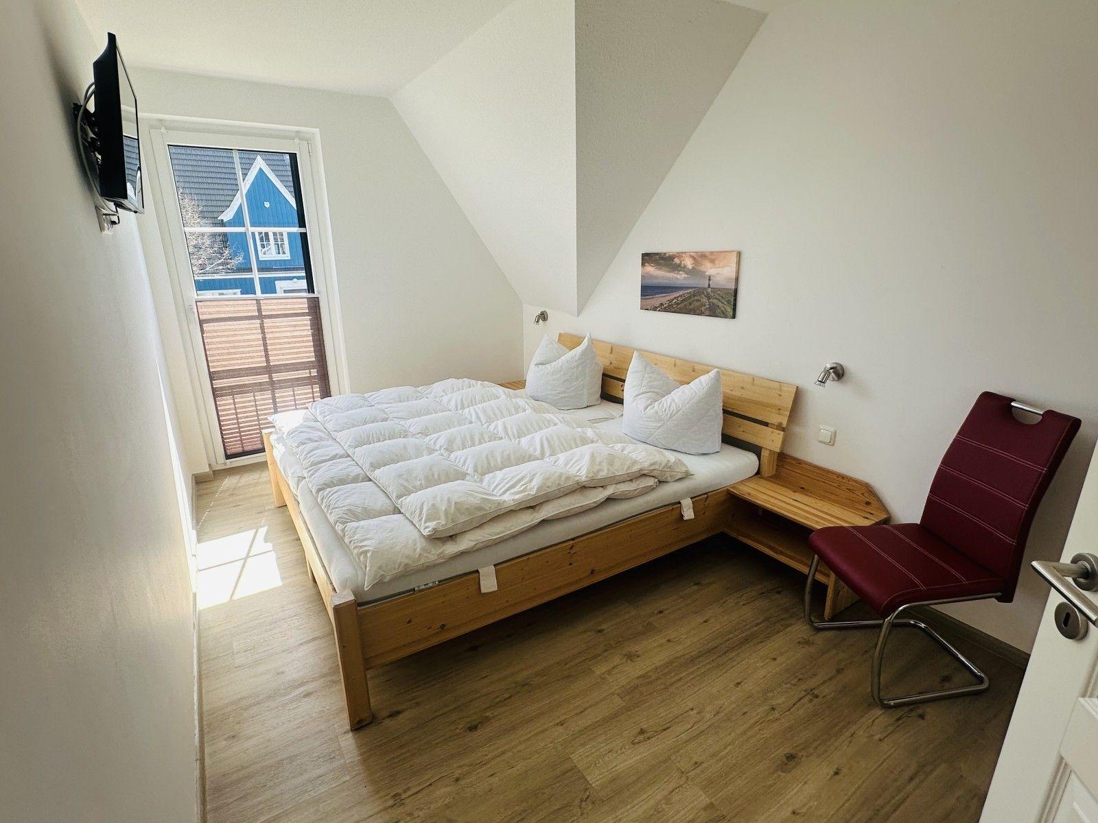 Schlafzimmer mit Doppelbett, Fenster und roter Sitzgelegenheit.