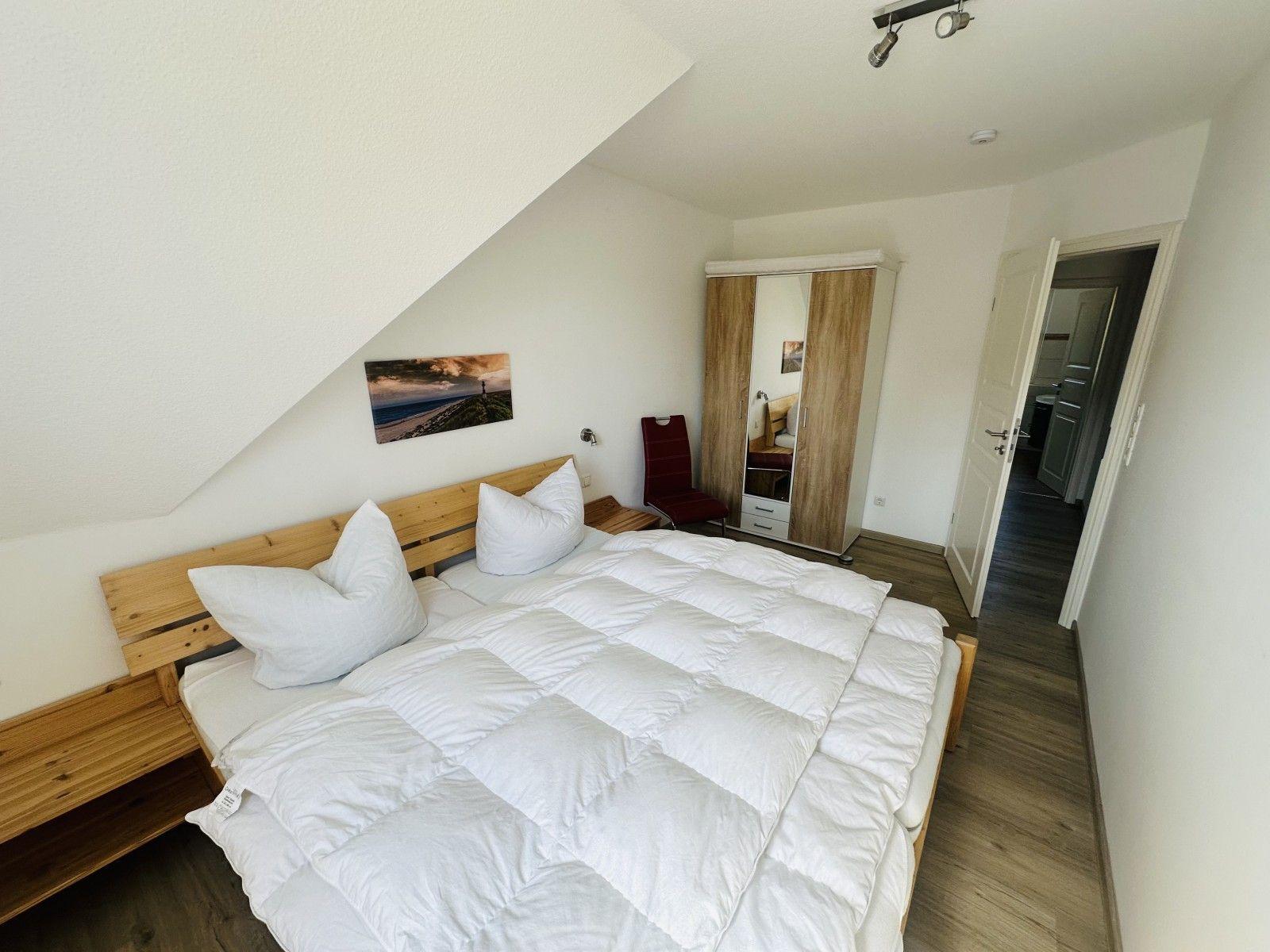 Schlafzimmer mit Doppelbett, Kleiderschrank und Wandbild unter Dachschräge.