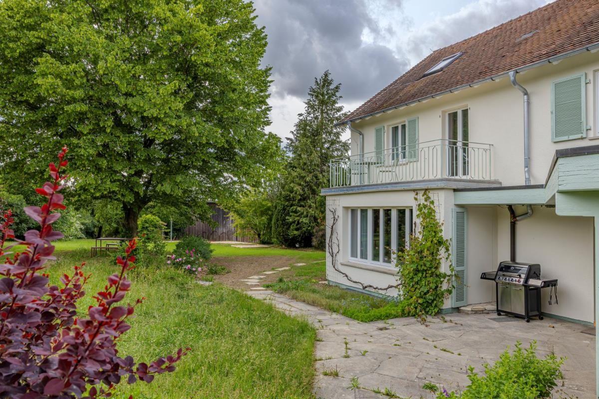 Haus mit Balkon, Grill und Gartenweg unter Bäumen.