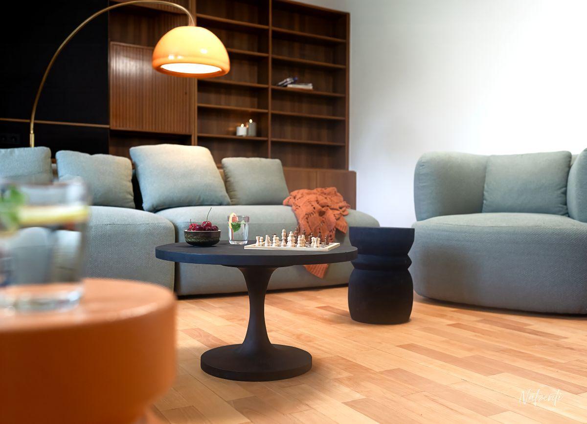 Ein Wohnzimmer mit grauen Sofas, einem runden Tisch und einem Bücherregal.