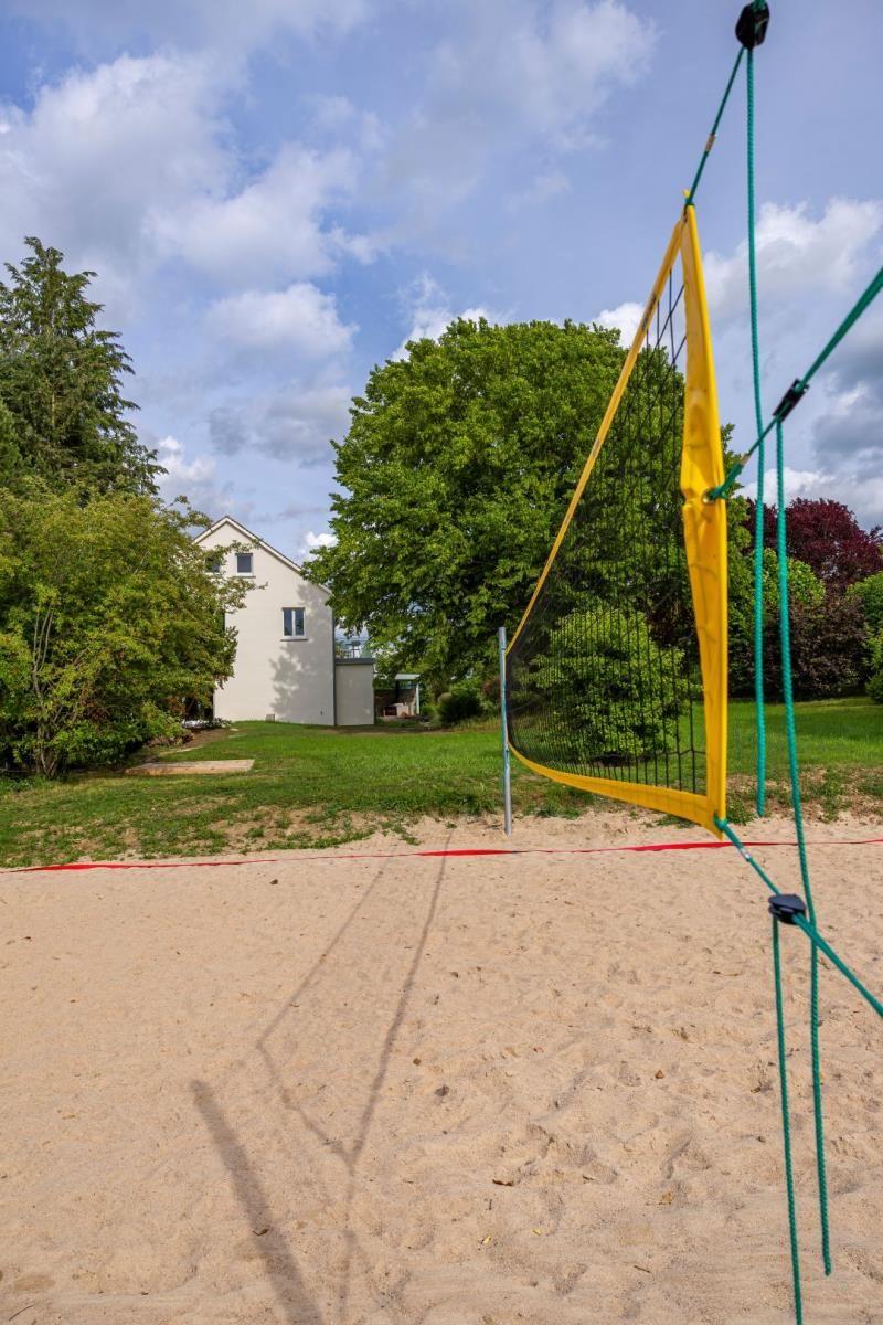 Sandplatz mit Volleyballnetz vor einem Haus im Grünen.
