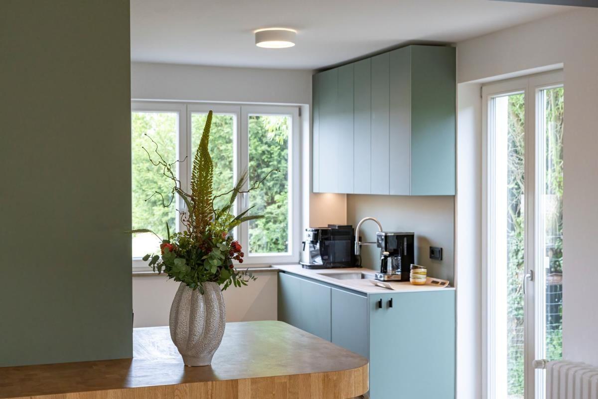Küche mit grünen Schränken, Fenster und Blumenvase auf Holzoberfläche