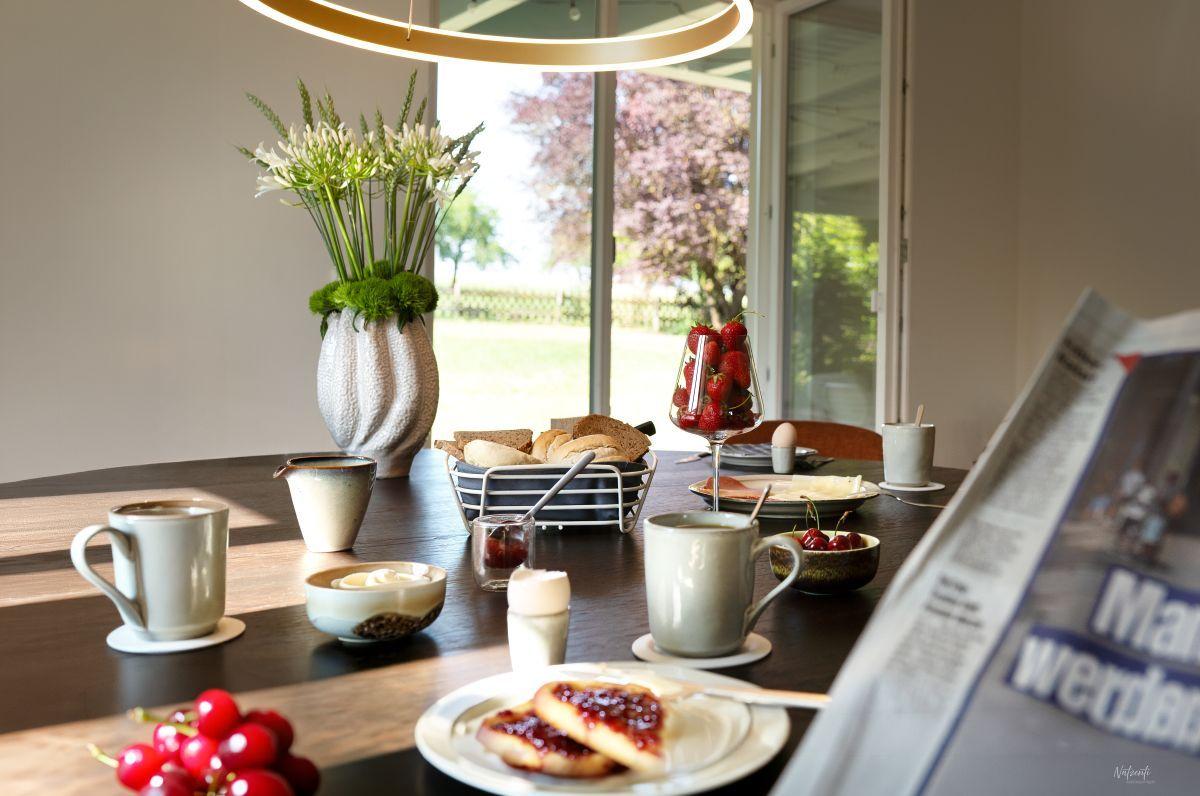 Frühstückstisch mit Kaffee, Obst und Zeitung vor Fenster