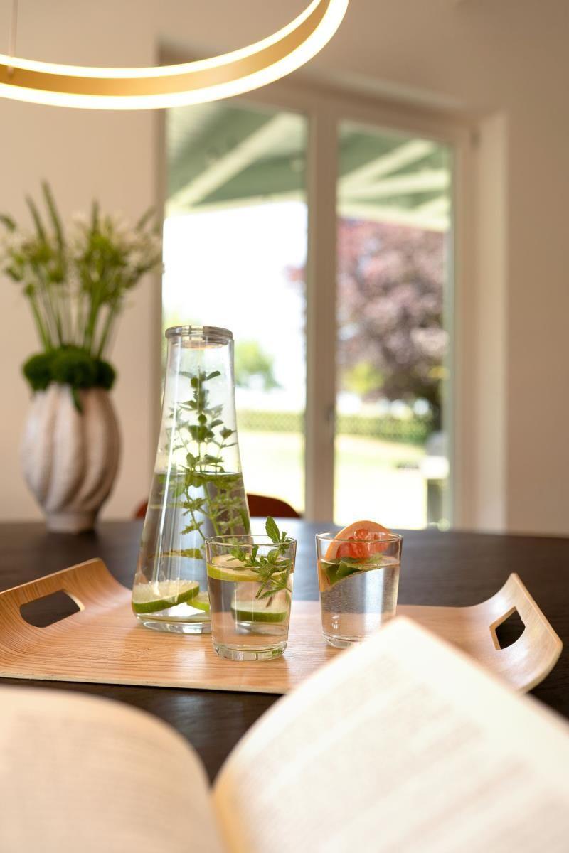Auf dem Tisch stehen Gläser mit Wasser und Zitrusfrüchten. Im Hintergrund ist ein Fenster zu sehen.