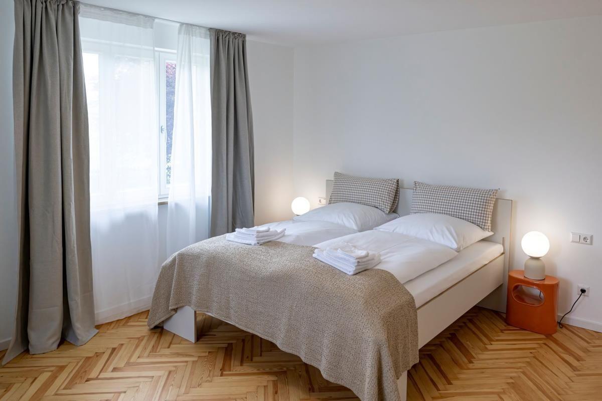 Schlafzimmer mit Doppelbett, Holzboden und Fenster mit Vorhängen.