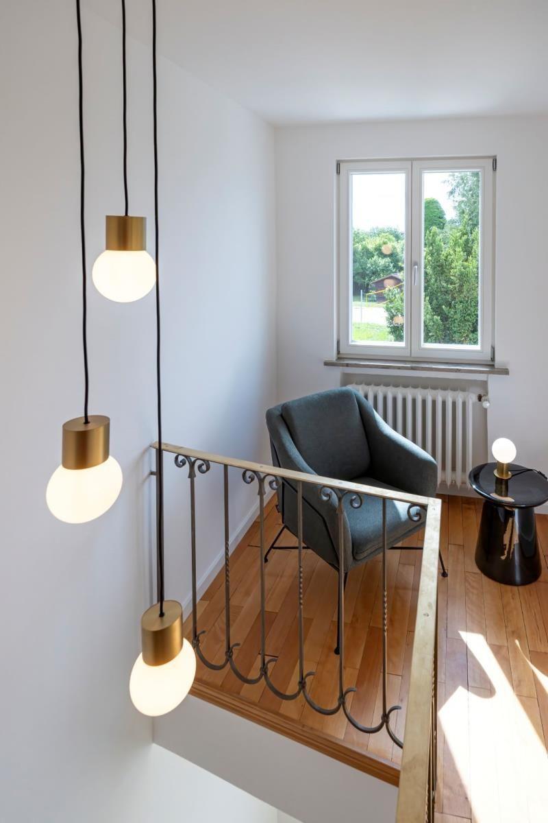 Lichtdurchfluteter Raum mit grauer Sitzgelegenheit und schmiedeeisernem Geländer.