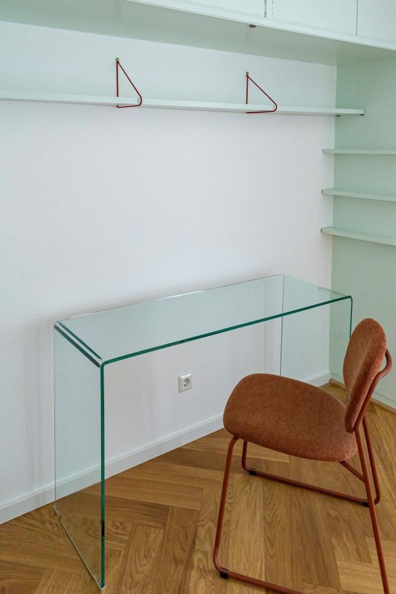 Glas-Tisch mit Stuhl vor Wandregal und Holzboden.
