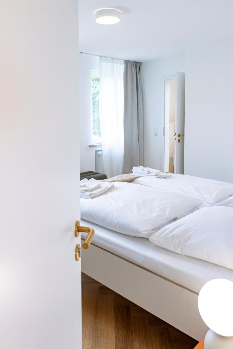 Schlafzimmer mit weißem Bett, Holzboden und Fenster mit Vorhängen.