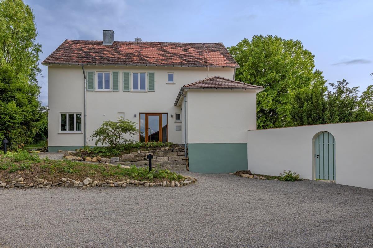 Ein zweistöckiges Haus mit rotem Dach, grünen Fensterläden und einem Kiesweg.