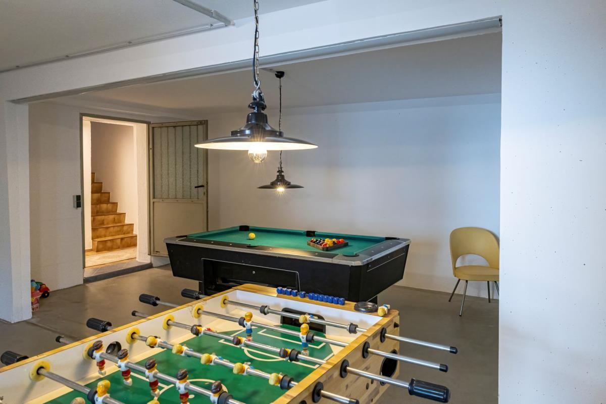 Raum mit Tischfußball und Billardtisch unter Hängelampen. Treppenhaus im Hintergrund.