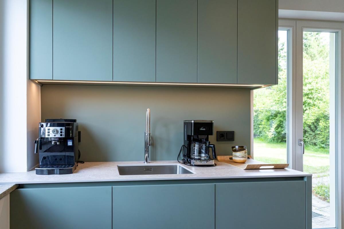 Küche mit grauen Schränken, Edelstahlspüle und Fenster zur grünen Außenseite.