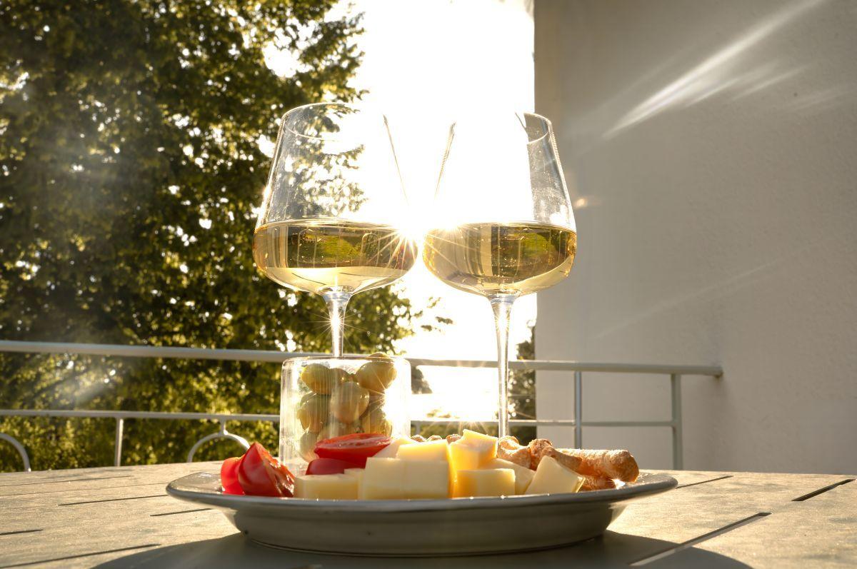 Zwei Weingläser und eine Platte mit Käse, Tomaten und Oliven auf einer Terrasse.