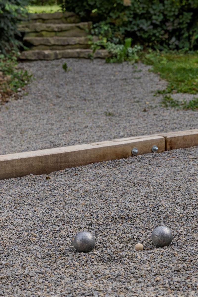 Pétanque-Bälle liegen auf Kies im Garten. Hintergrund: Steinstufen und Vegetation.