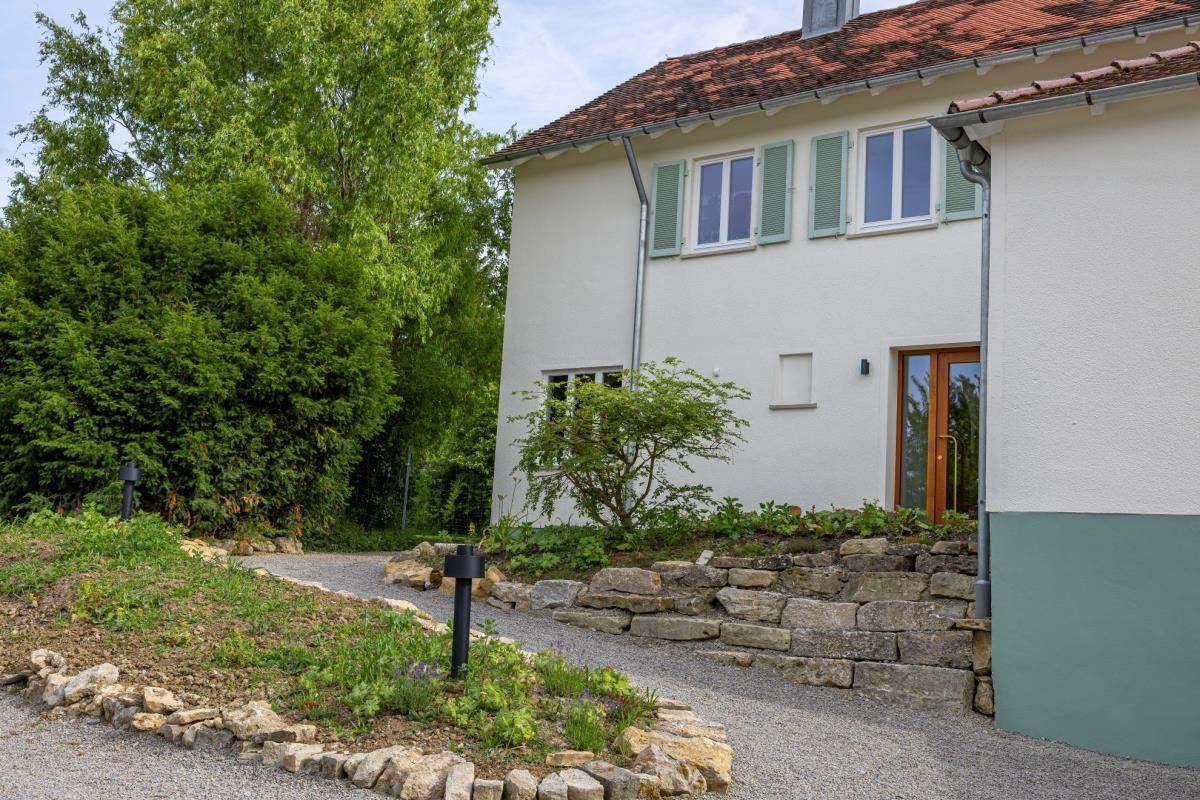 Ein zweistöckiges Haus mit weißer Fassade, grünen Fensterläden und einem Steinweg.
