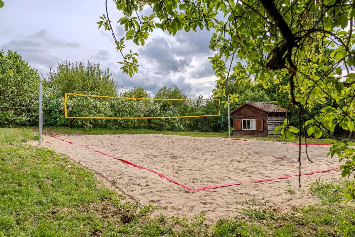 Sandplatz mit Volleyballnetz und kleinem Holzhaus im Hintergrund.