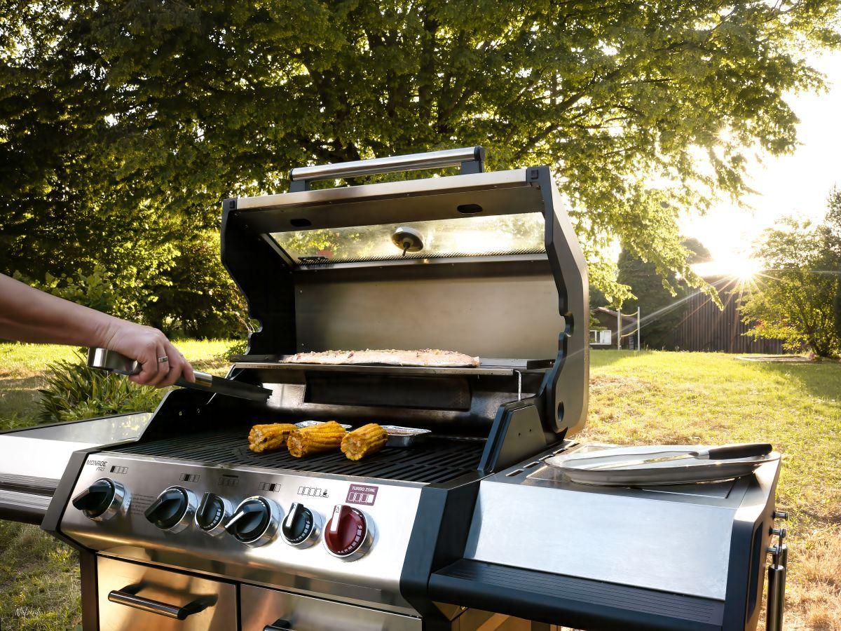 Grill mit Mais und Fisch im Garten bei Sonnenuntergang.