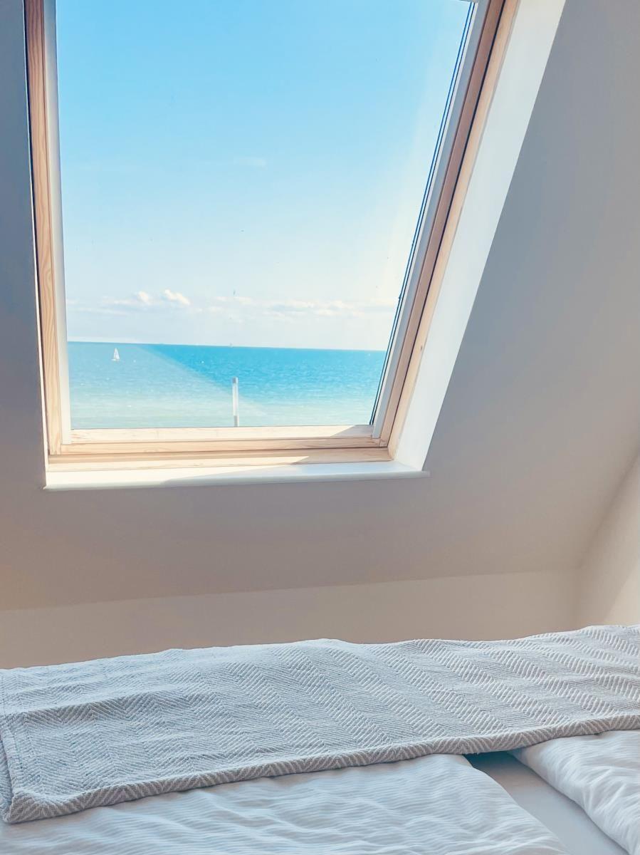 Dachfenster mit Blick auf das Meer und einen Segler.