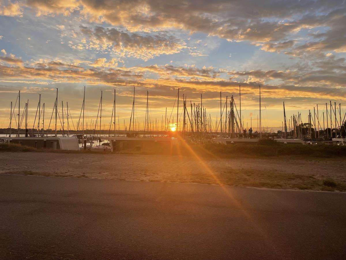 Sonnenuntergang über einem Yachthafen mit Masten und Wasser.