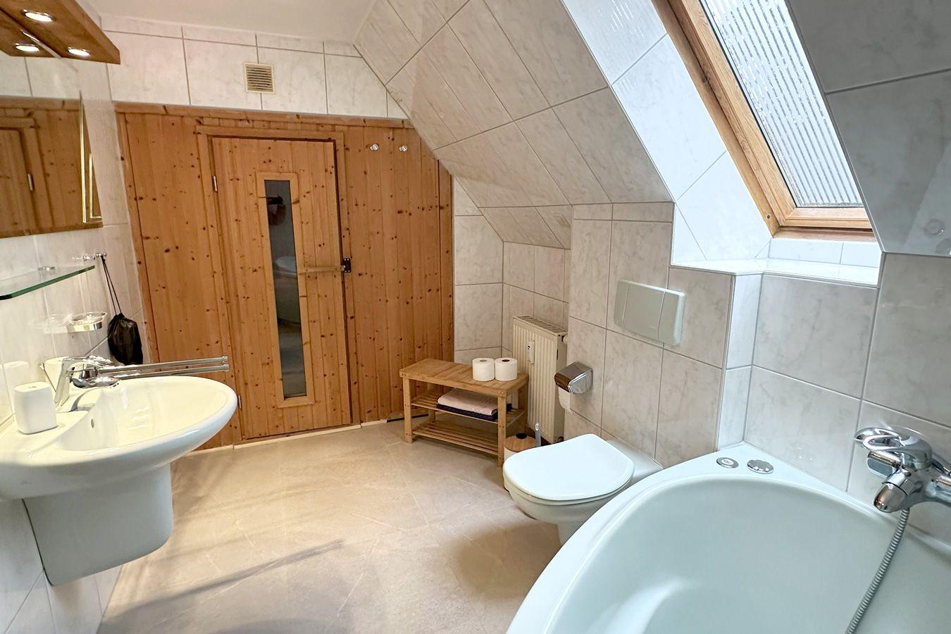 Badezimmer mit Dusche, Toilette und Badewanne unter Dachschräge mit Holztür.