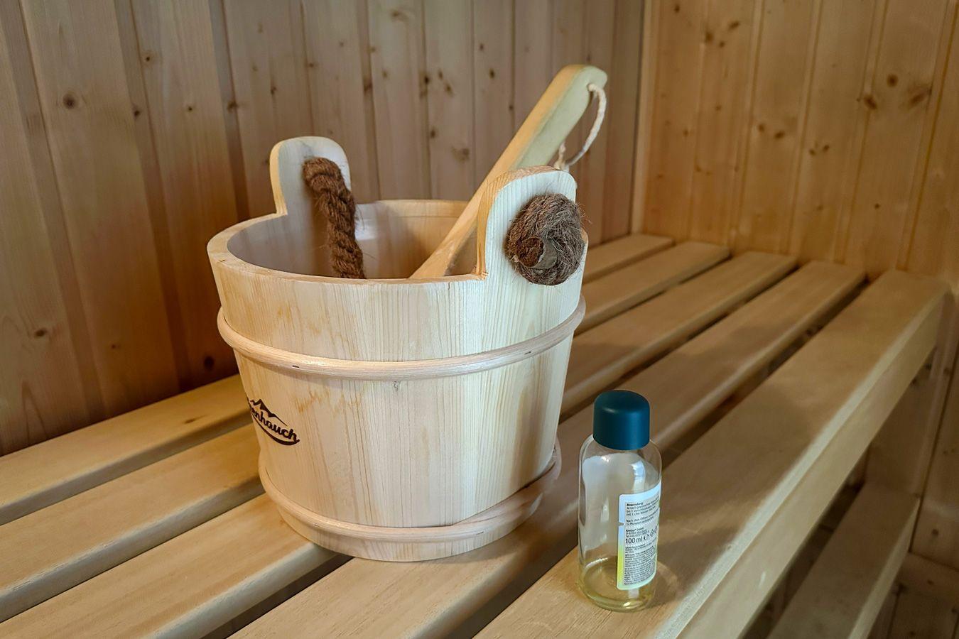 Holzbadewanne mit Besen und Flasche auf Sitzbank in Sauna.