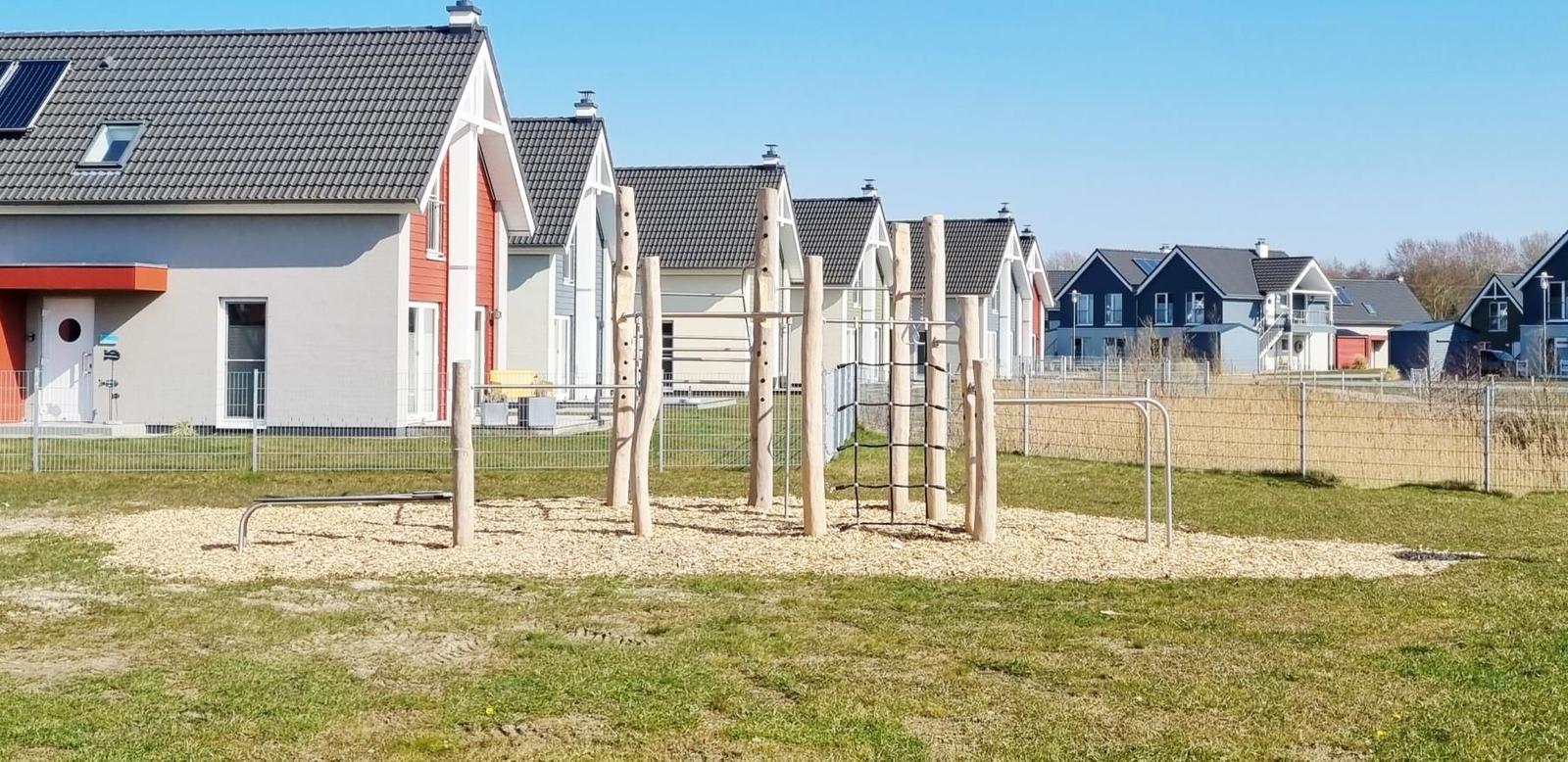 Kinder-Spielplatz mit Holzgerüsten und Kletterelementen auf einem Sandbett vor modernen Häusern.
