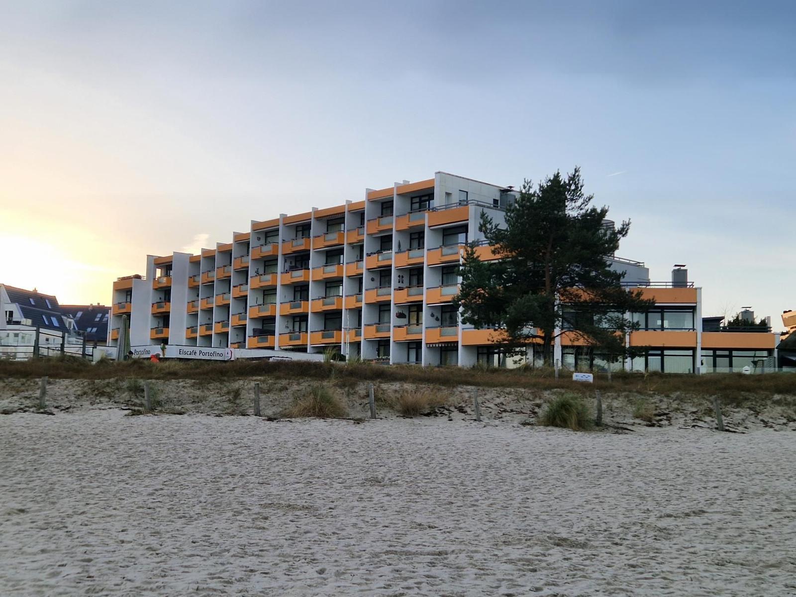 Strandvorsprung mit modernem Mehrfamilienhaus mit Balkonen und Sandstrand im Vordergrund.