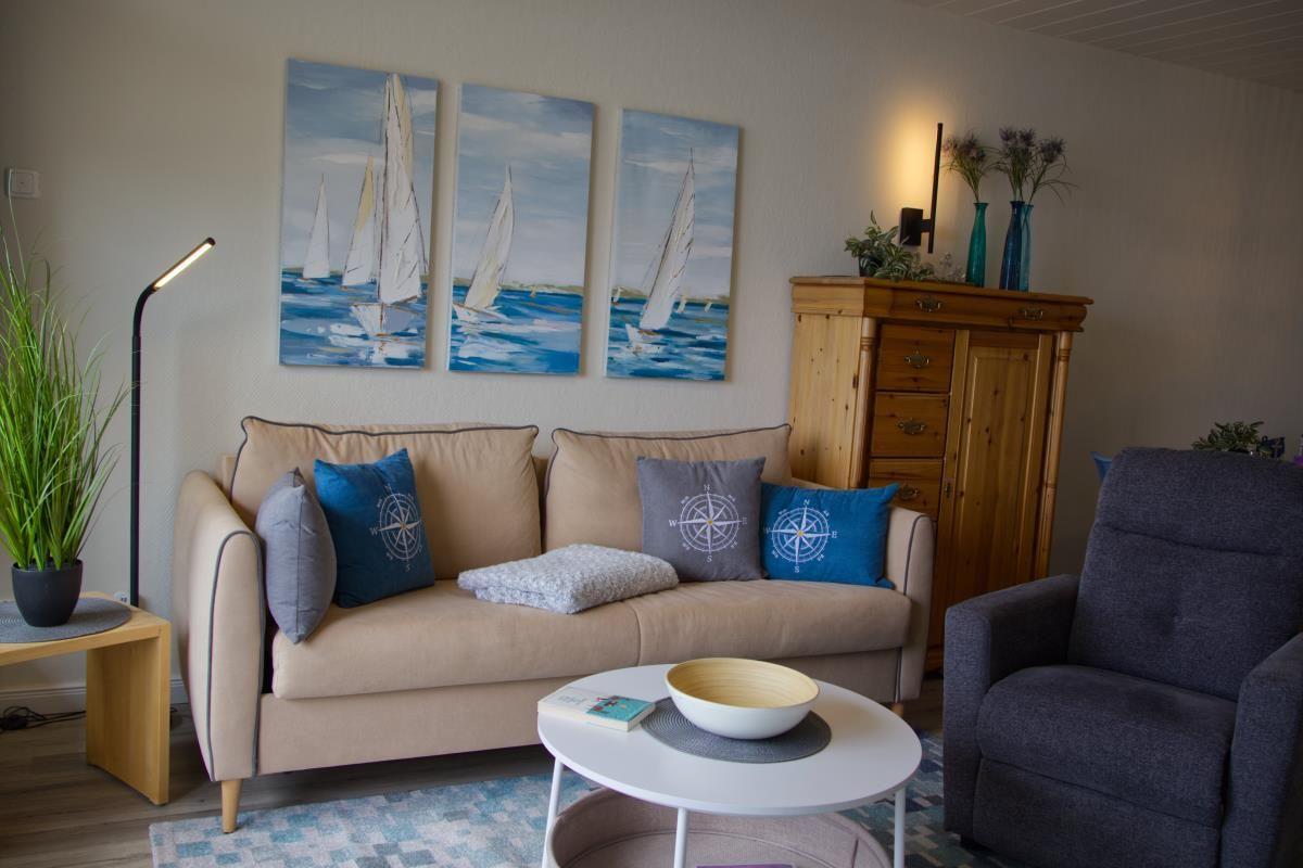 Wohnzimmer mit Sofa, Kissen, Couchtisch und Wandbildern von Segelbooten.