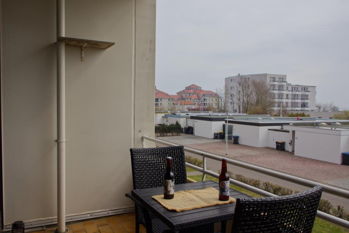 Terrasse mit Tisch und zwei Stühlen, zwei Flaschen darauf. Blick auf Gebäude und Grünfläche.