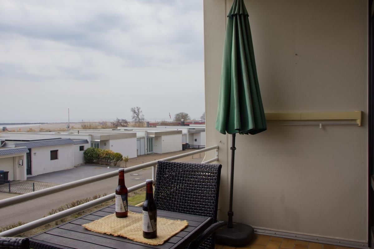 Terrasse mit Tisch, Stühlen und grünem Sonnenschirm. Blick auf Gebäude und Fläche.
