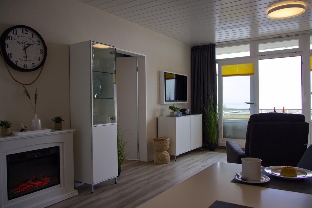 Wohnzimmer mit Fernseher, elektrischem Kamin und Blick auf Balkon.