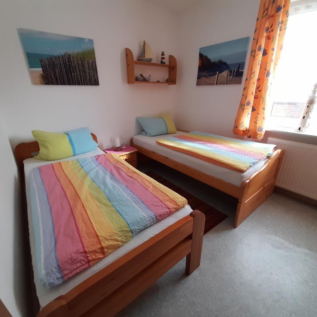Two single beds with colorful bedding, wall pictures, and window with curtains.