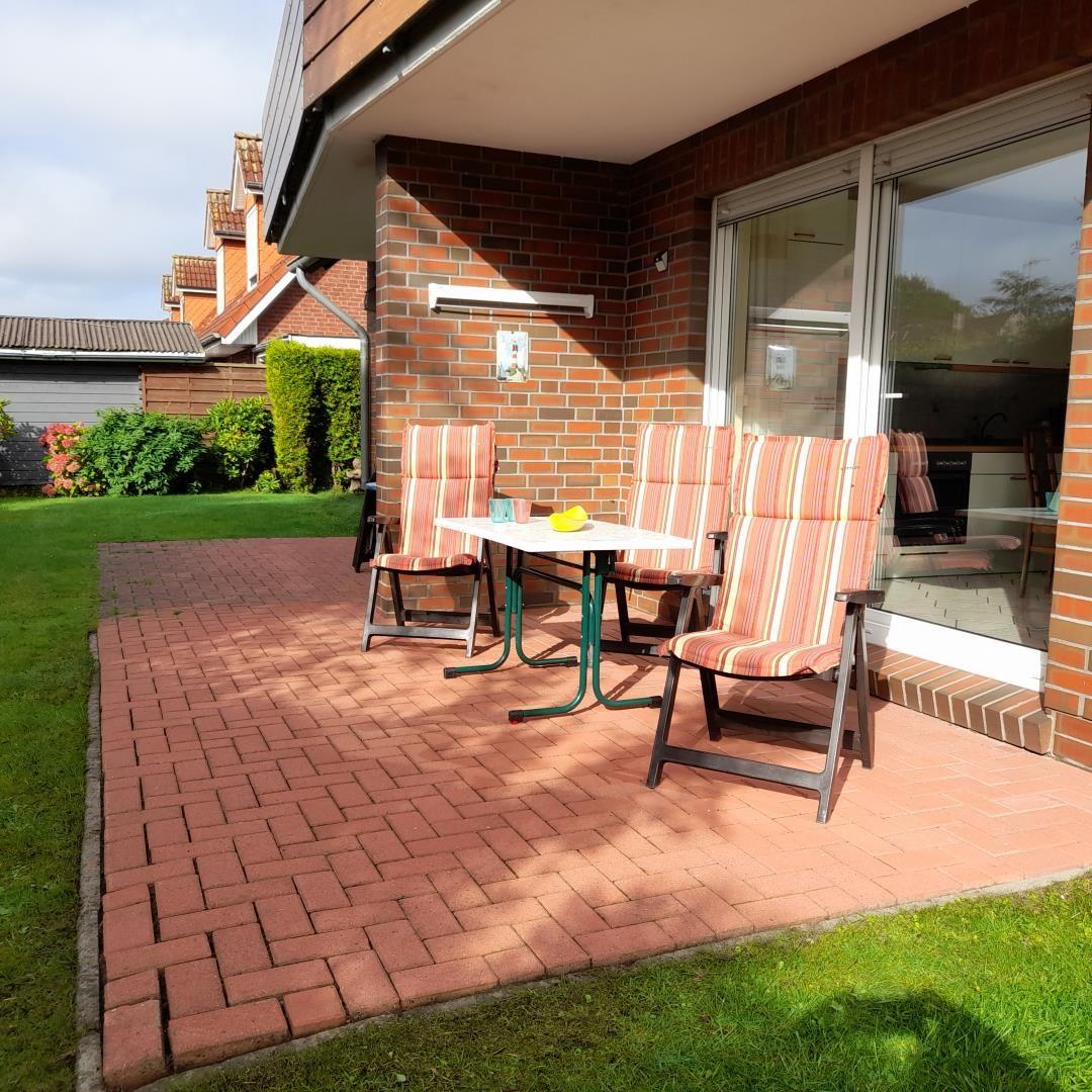Terrace with table and three chairs, surrounded by grass and bricks.