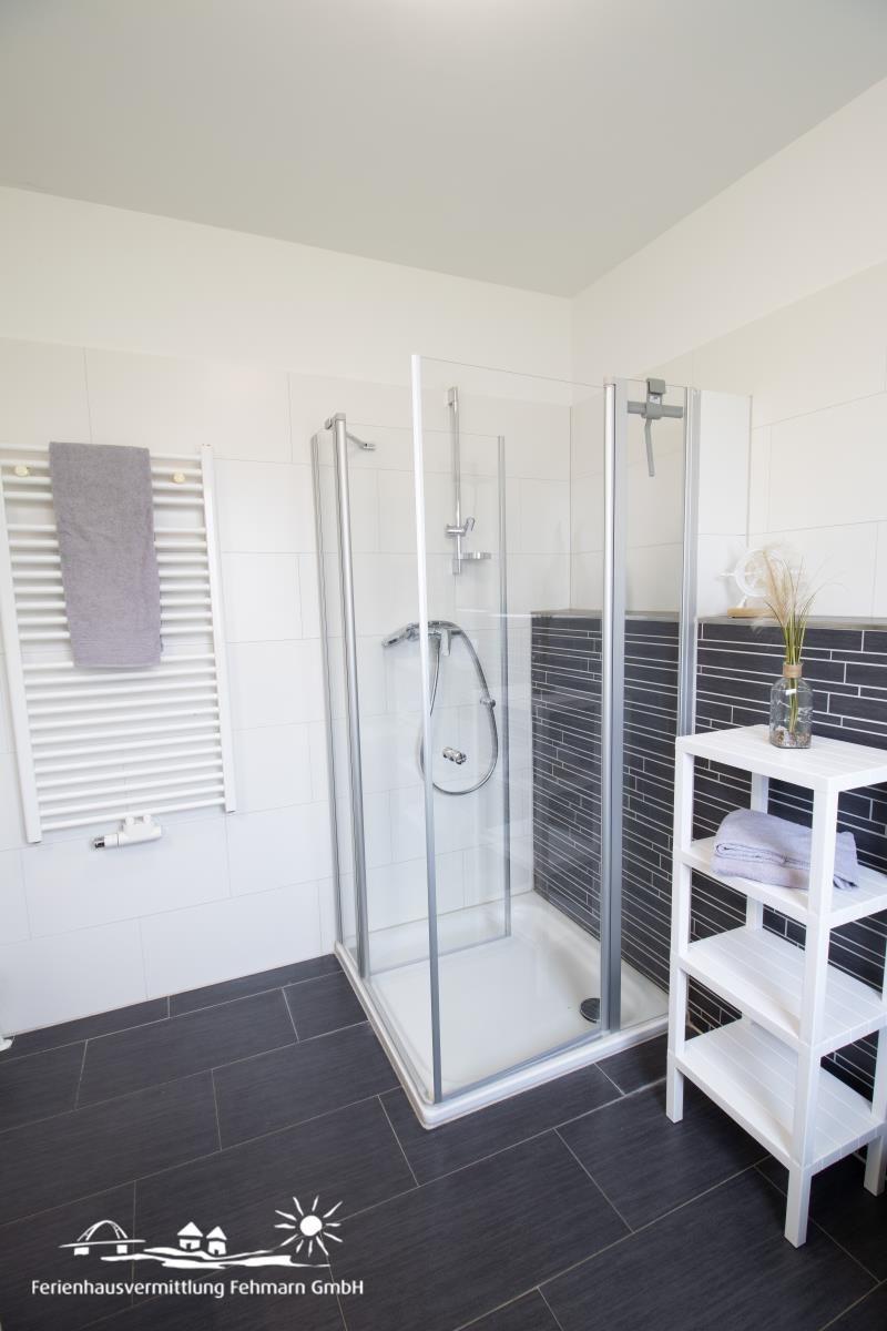 Badezimmer mit Dusche, Heizkörper und Holzregal.